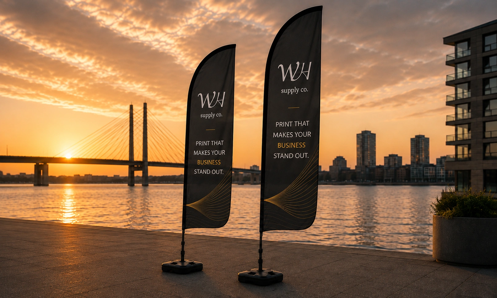 Two black beach flags with WH Supply Co. branding by the waterfront at sunset.